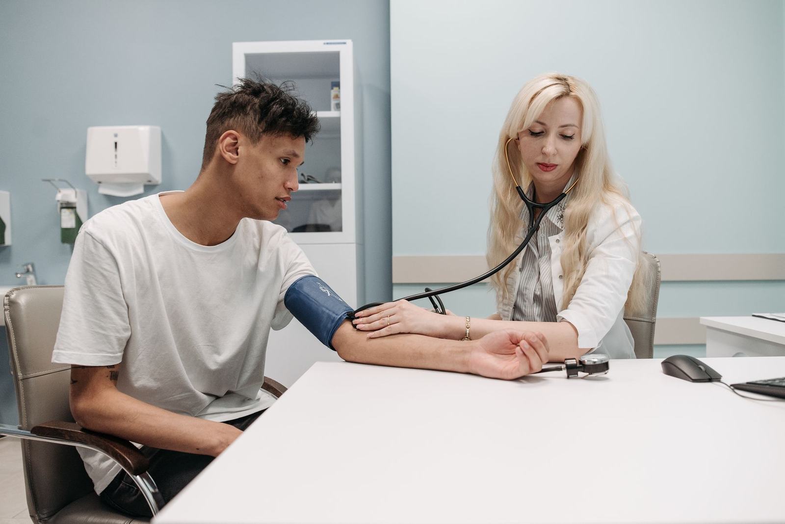 A clinician checks a young man's blood pressure in a bright exam room